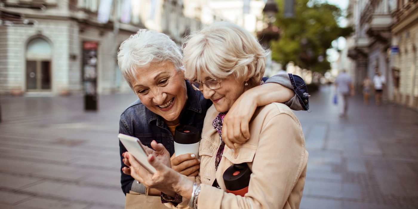 Close up of two female senior friends using a phone while having a walk in the city