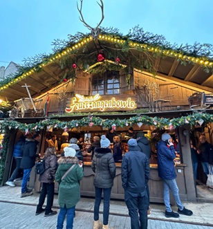 A festive gathering of people enjoying a charming Christmas market adorned with twinkling lights and seasonal decorations.
