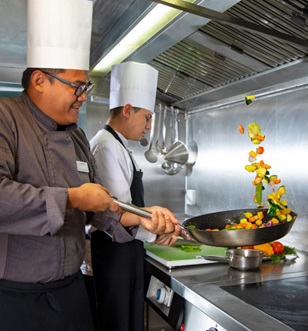 Two chefs skilfully sauté vibrant vegetables in a gleaming pan, showcasing culinary artistry and fresh ingredients.