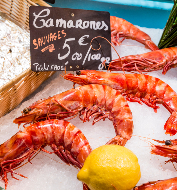 King prawns scatted on a bed of crushed iced accompanied by a whole lemon and a chalk board stating the price,