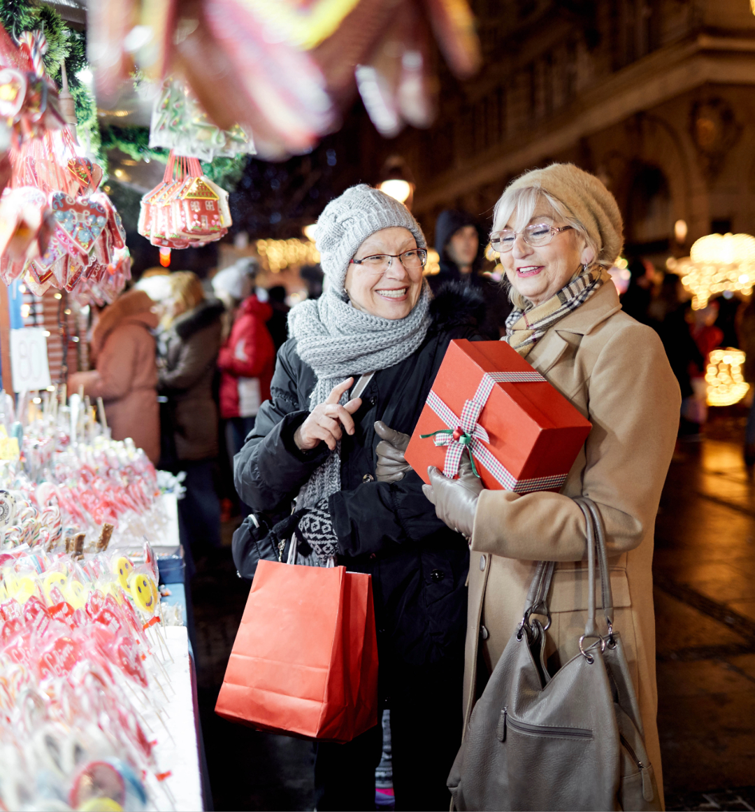 Two ladies holding gifts browsing products at a Christmas market stall