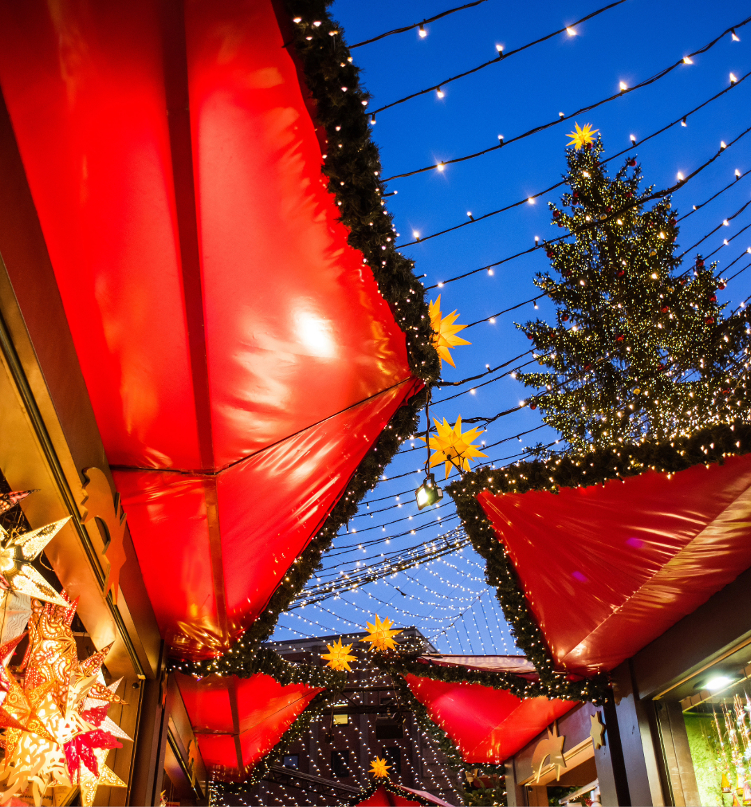 Looking up at night sky from christmas market stall with lights and tree seen above