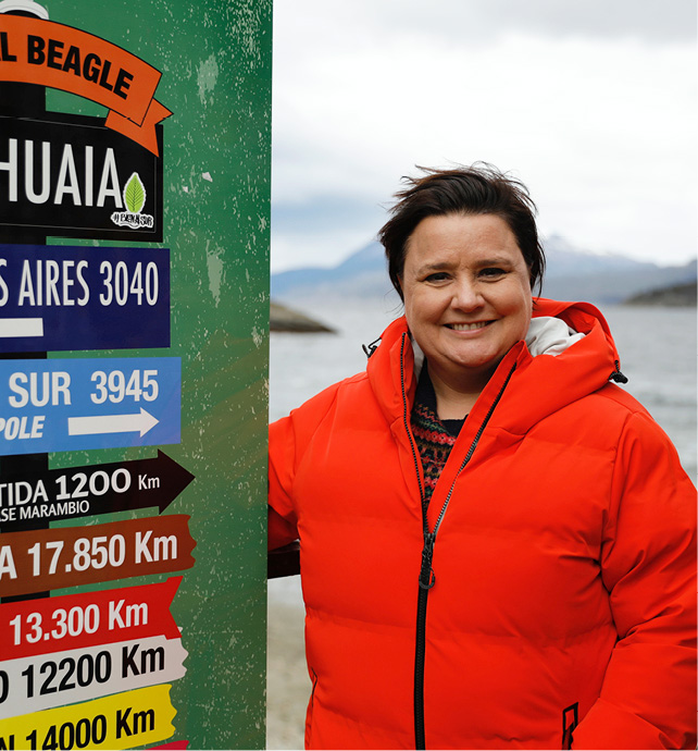 Scottish comedian, television presenter, writer and panellist Susan Calman standing next to a sign wearing a vibrant red puffer jacket