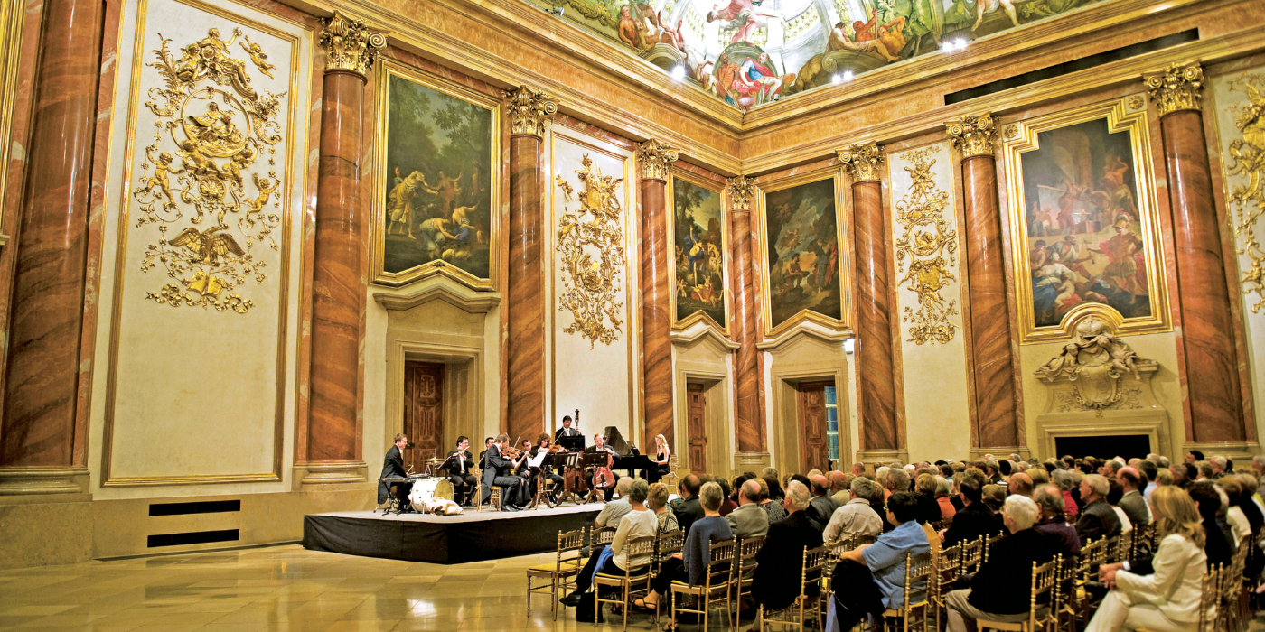 The expansive Palais Liechenstein room highlighted by a stunning ceiling painting, displaying artistic craftsmanship and captivating imagery.