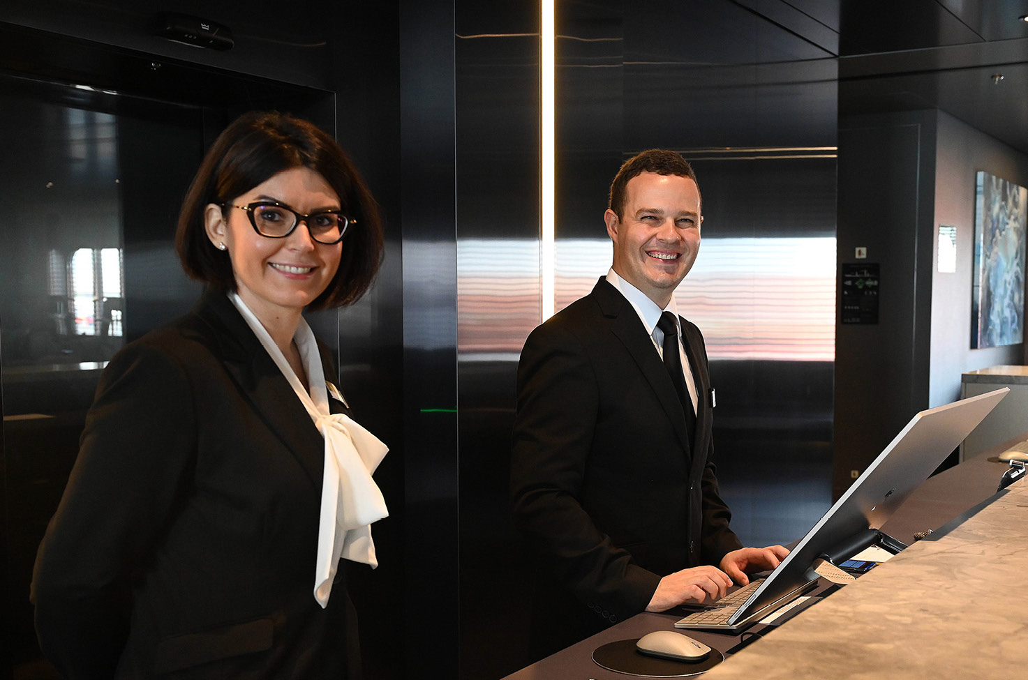 two receptionists standing at a desk and smiling