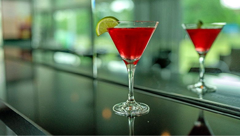 Red cocktail with a lime wedge garnish on a bar table