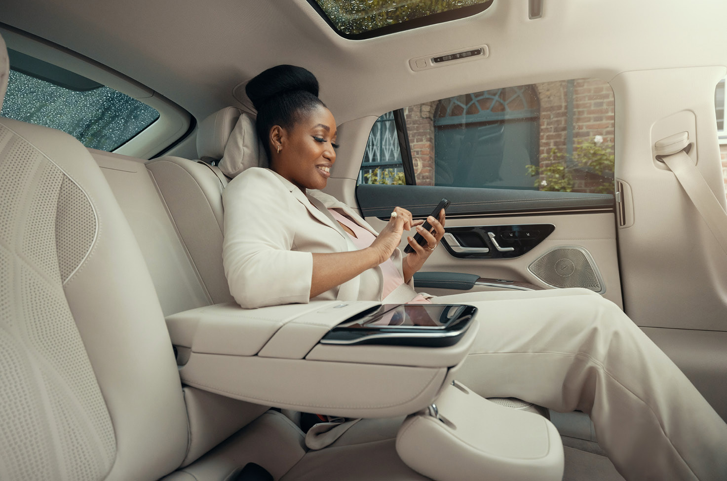 Passenger on her phone in the back seat of a Blacklane Private Chauffeur Service luxury vehicle with beige interior