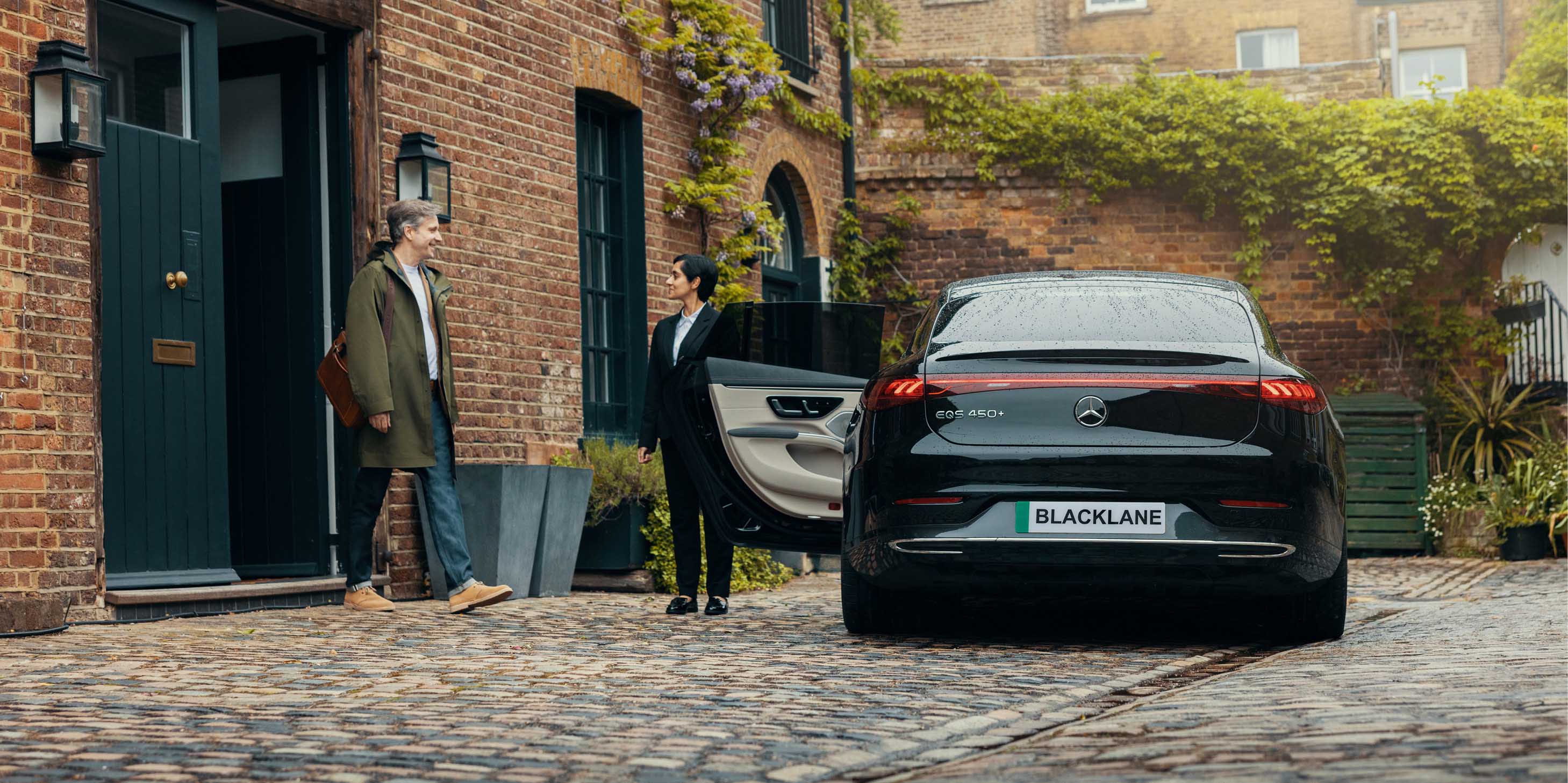 Blacklane Private Chauffeur Service driver holding door open door for a passenger to get into a black luxury sedan vehicle