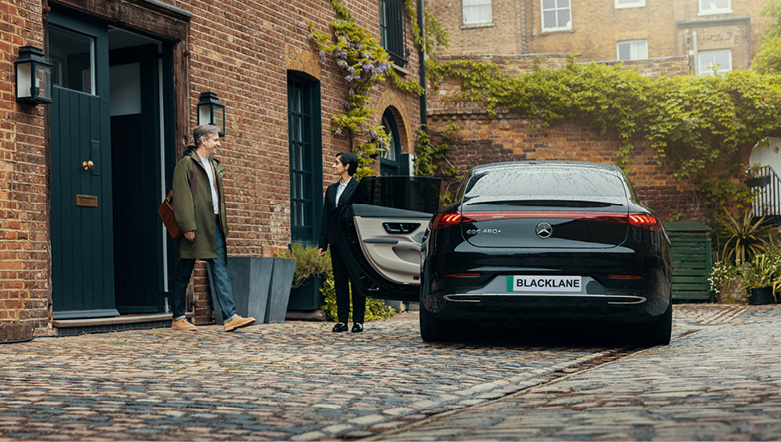 Blacklane Private Chauffeur Service driver holding door open door for a passenger to get into a black luxury sedan vehicle