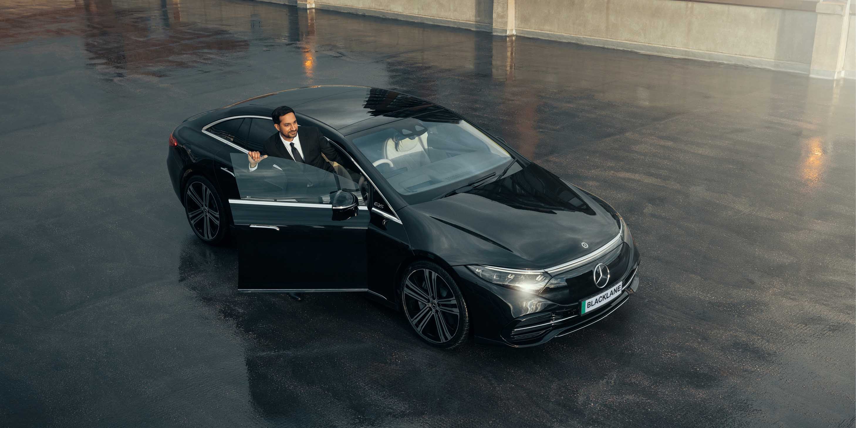 Chauffeur driver wearing a suit stepping out of the door of a luxury black vehicle