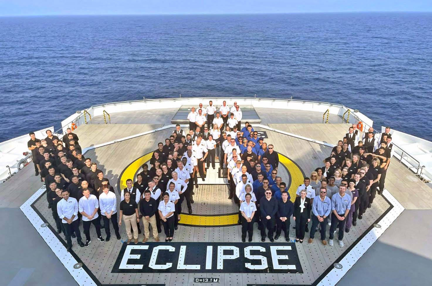 group of people on a helipad posed in a W formation